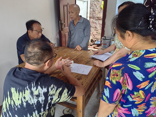 《信手拈來》。7月21日，重慶市二零八地質(zhì)環(huán)境研究院有限公司勘察分院水文地質(zhì)所所長兼潼南區(qū)駐守負(fù)責(zé)人王克峰與潼南區(qū)規(guī)劃和自然資源局梓潼所負(fù)責(zé)人米澤坤，在梓潼街道社區(qū)一戶農(nóng)戶家里給戶主介紹如何做好房前屋后邊坡防治，王克峰隨手用筆在手上畫出邊坡輪廓。李鋒俊攝