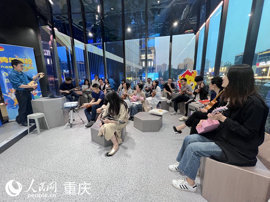 九龍坡區(qū)萬(wàn)象書屋圓形劇場(chǎng)區(qū)里，學(xué)員們聚精會(huì)神聆聽老師講解尤克里里的構(gòu)成。 人民網(wǎng)記者 胡虹攝