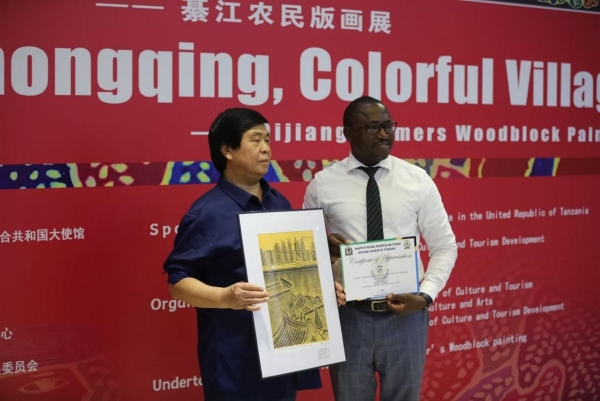 綦江農(nóng)民版畫院院長桂煥勇手持楊榮作品《開放中的重慶》與坦桑尼亞國家博物館執(zhí)行館長合影。重慶文藝職院供圖