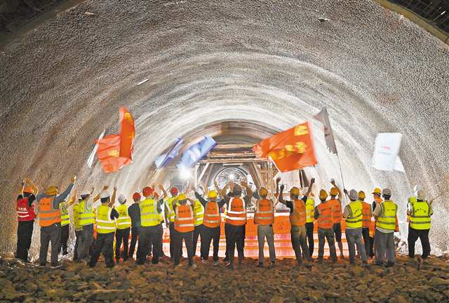 圖為建設(shè)者在塔平村隧道貫通點(diǎn)向?qū)γ婢蜻M(jìn)工友搖旗慶祝。